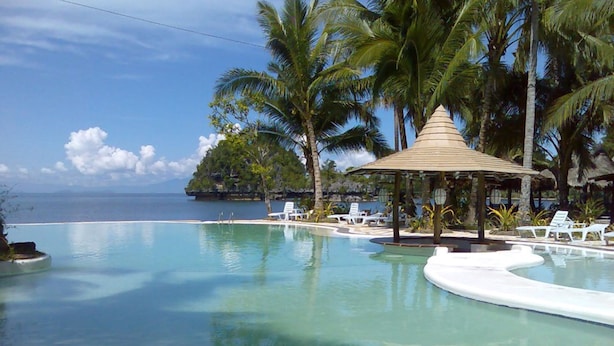 A clear blue infinity pool with lounge chairs and a palm tree, surrounded by a wooden deck and a small gazebo. - Caluwayan Palm Island Resort (Marabut)