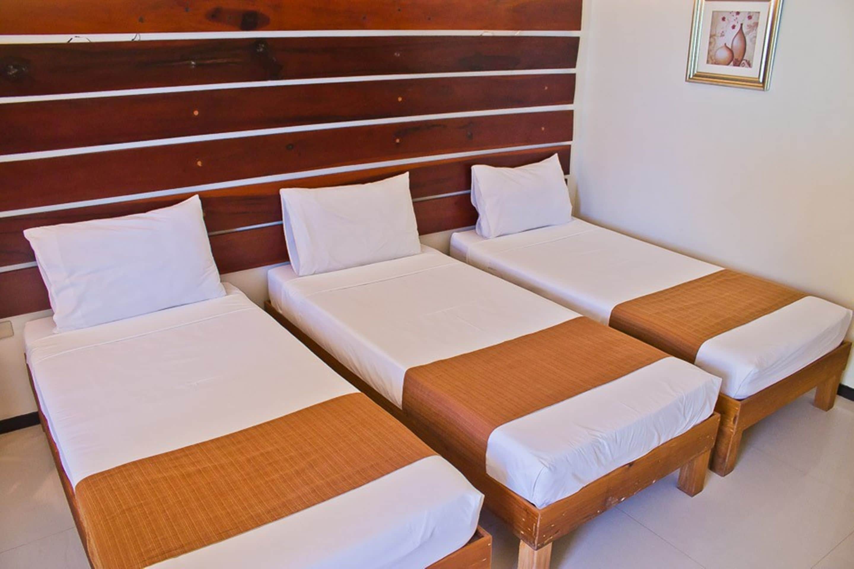 A hotel room with three single beds, each with white bedding and a brown headboard.
