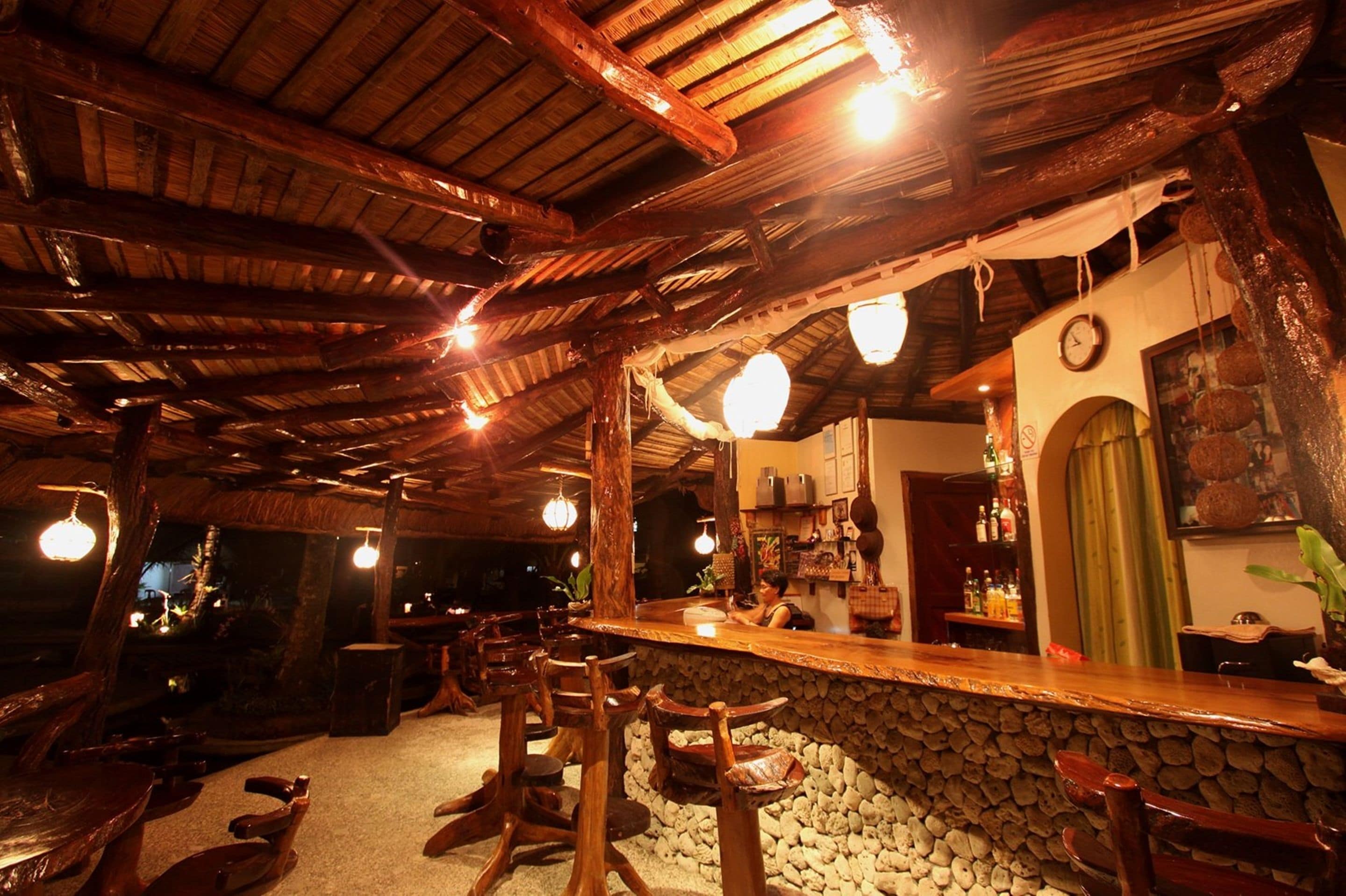 A rustic bar area with wooden furniture and a stone wall backdrop.