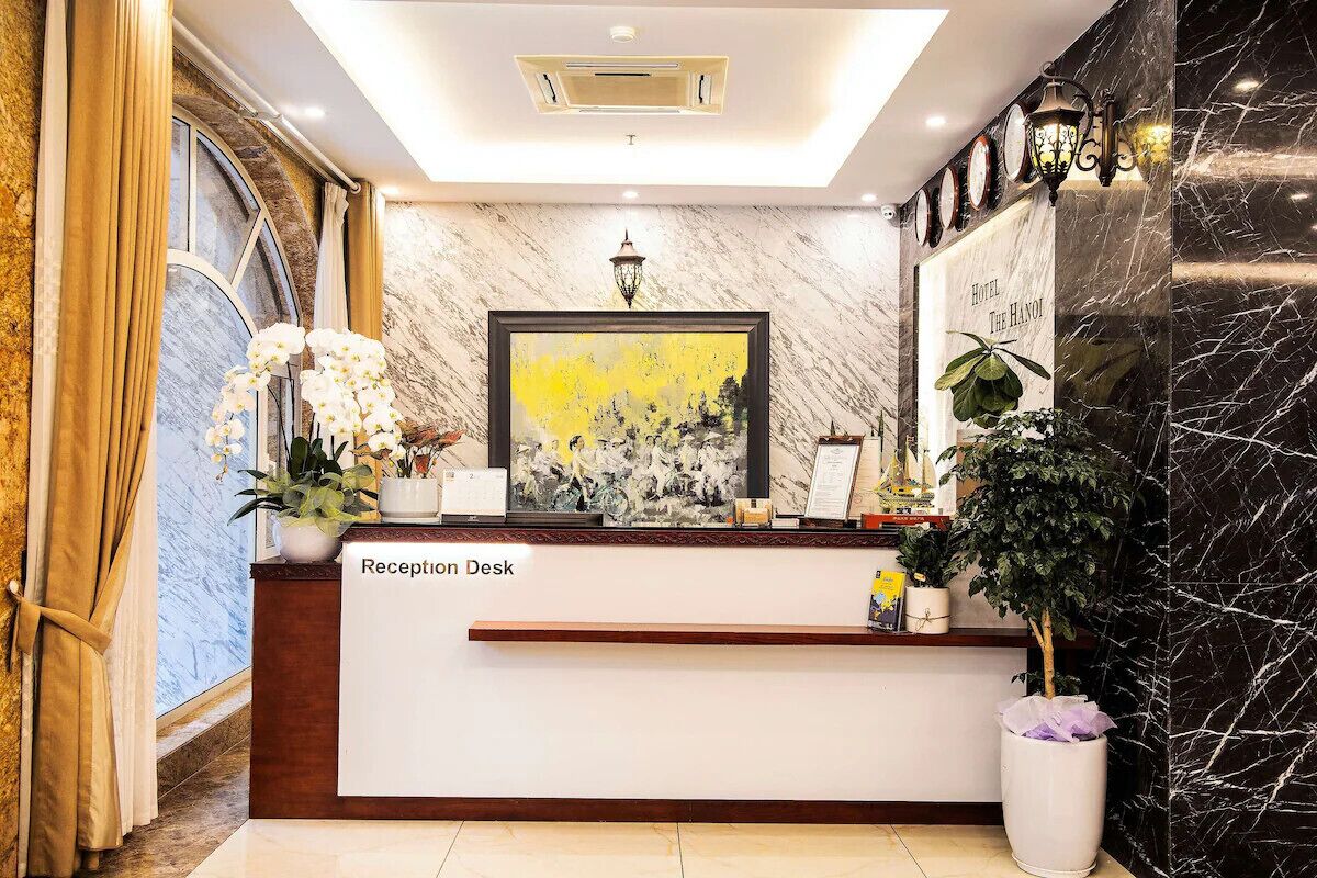 A reception desk with a marble wall, a framed painting, and a potted plant.