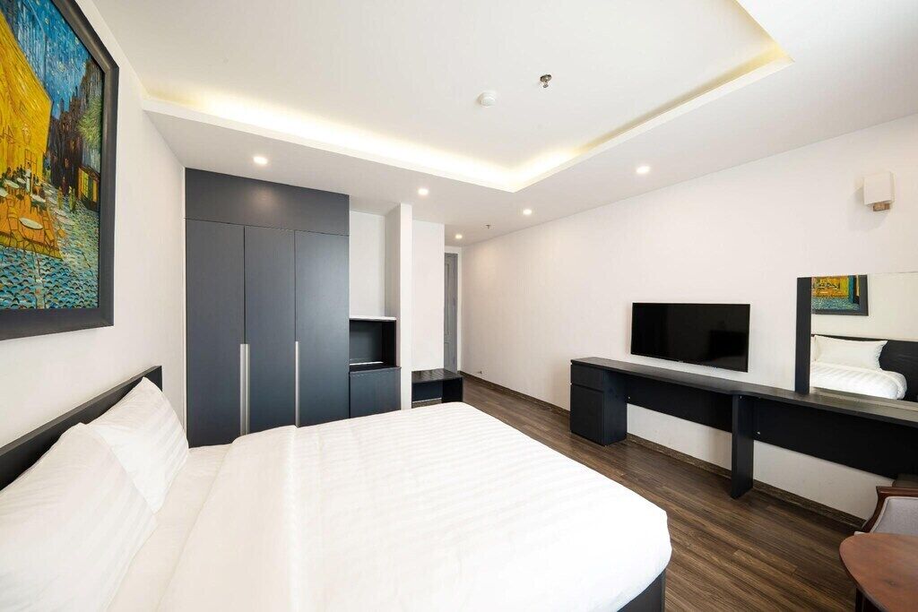 A modern hotel room with a large bed, a desk with a flat-screen TV, a wardrobe, and a painting on the wall.