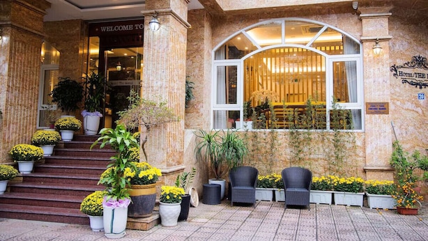 Entrada de hotel con un arco imponente, escalones que conducen a la puerta y plantas en macetas.