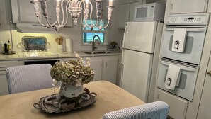 Una cocina con una mesa de comedor, sillas, una araña, un refrigerador y un microondas.