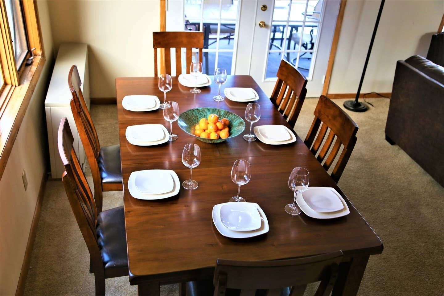 A dining table set for four with chairs, a bowl of fruit, and wine glasses.