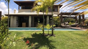 Una casa de dos pisos con piscina, rodeada de palmeras y un césped bien cuidado.