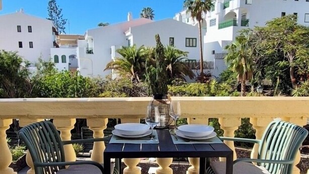 A balcony with a table set for two, surrounded by greenery and white buildings in the background. - Entire apartment in Costa Adeje (Costa Adeje)