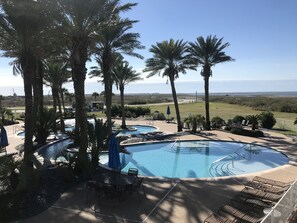 A pool area with multiple pools, lounge chairs, and palm trees. - Shores N Sunsets, beautiful Pointe West Galveston Bay & Beaches (Galveston)