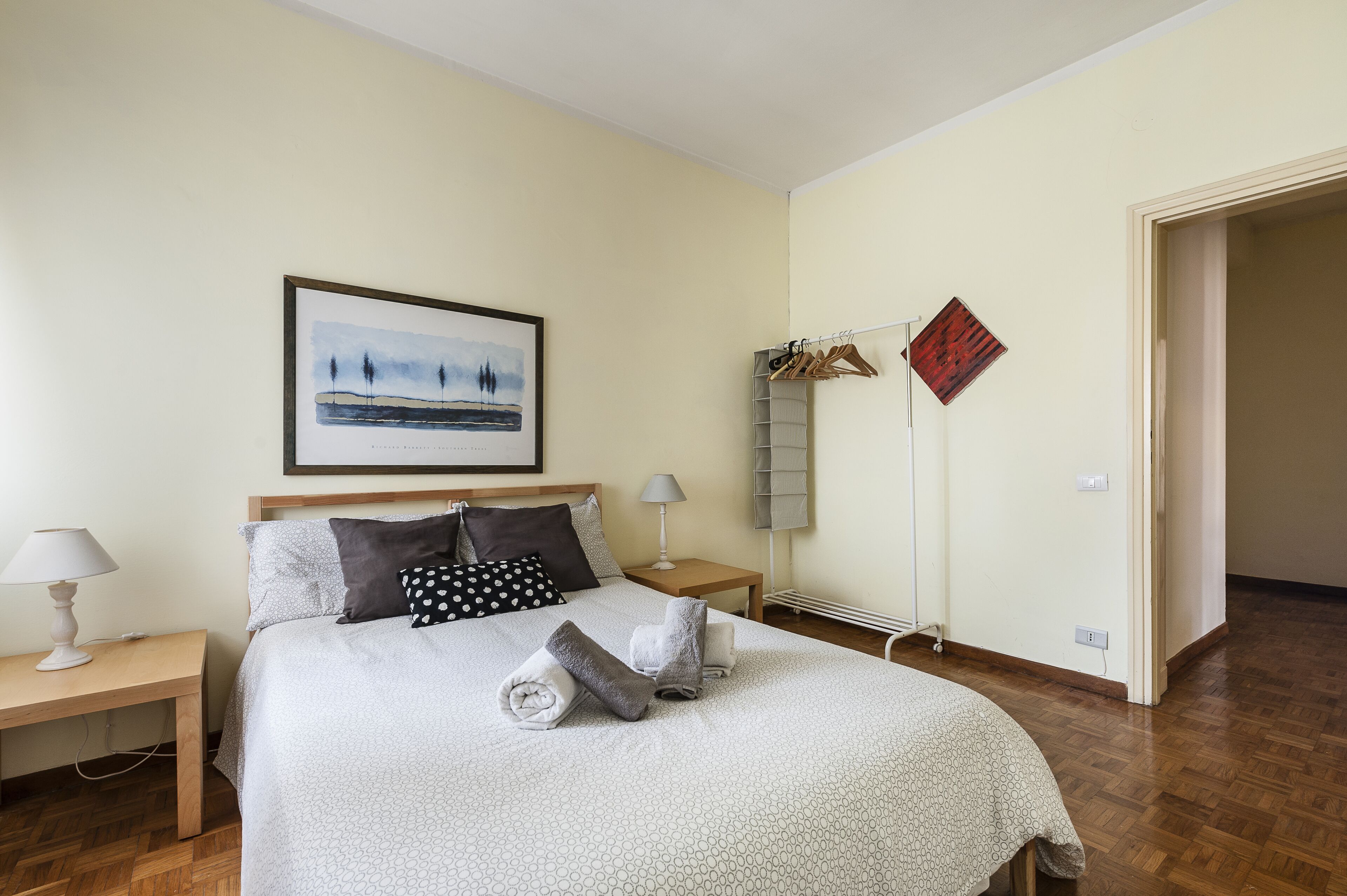 Une chambre à coucher bien rangée, avec un lit, deux tables de chevet, un tableau encadré et un porte-manteau.