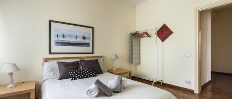 Une chambre à coucher bien rangée, avec un lit, deux tables de chevet, un tableau encadré et un porte-manteau.