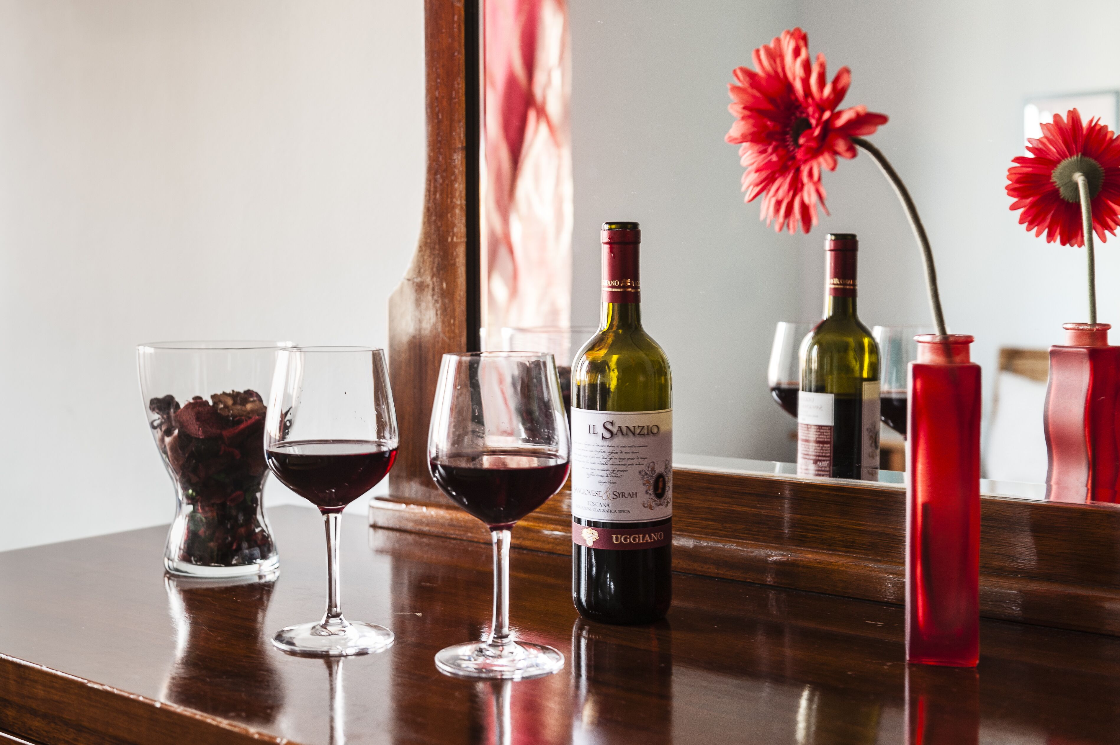 Un área de bar con copas de vino, botellas y un jarrón con flores.