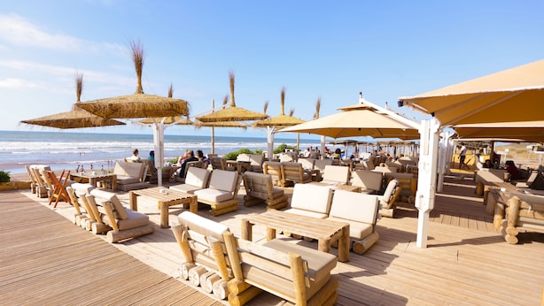 Une terrasse en bois avec des chaises longues et des parasols, offrant une vue sur l’océan.