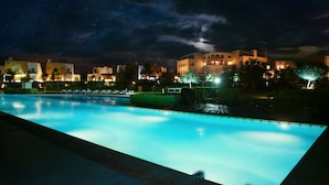 Une vue nocturne d’une piscine et des bâtiments adjacents, dont certains ont des fenêtres illuminées.
