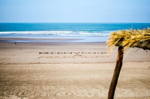 A beach with 'BIENVENUE AZTECA' written on the sand, a palm tree, and the ocean in the background.