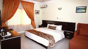 A hotel room with a bed, a desk with a kettle, a chair, and a ceiling fan. - Ishakool Hotels (Abuja)