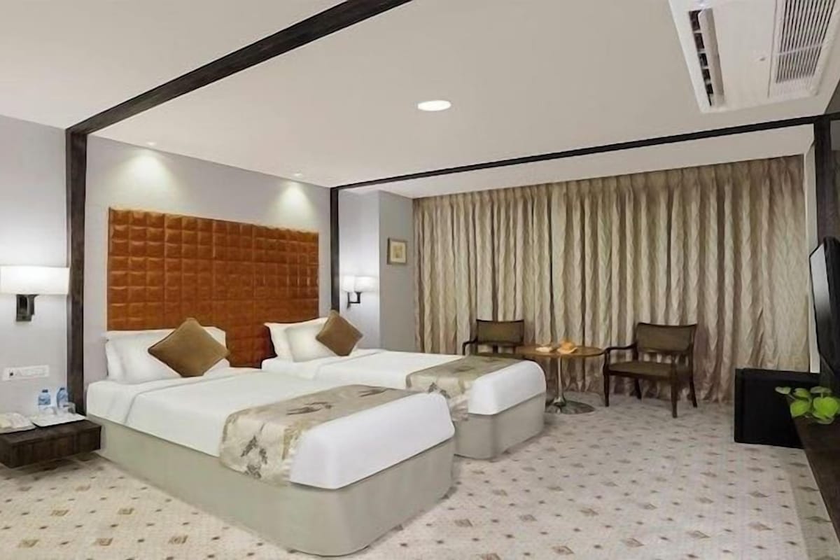 Une chambre d’hôtel avec deux lits, un bureau, une chaise, une télévision et un rideau.