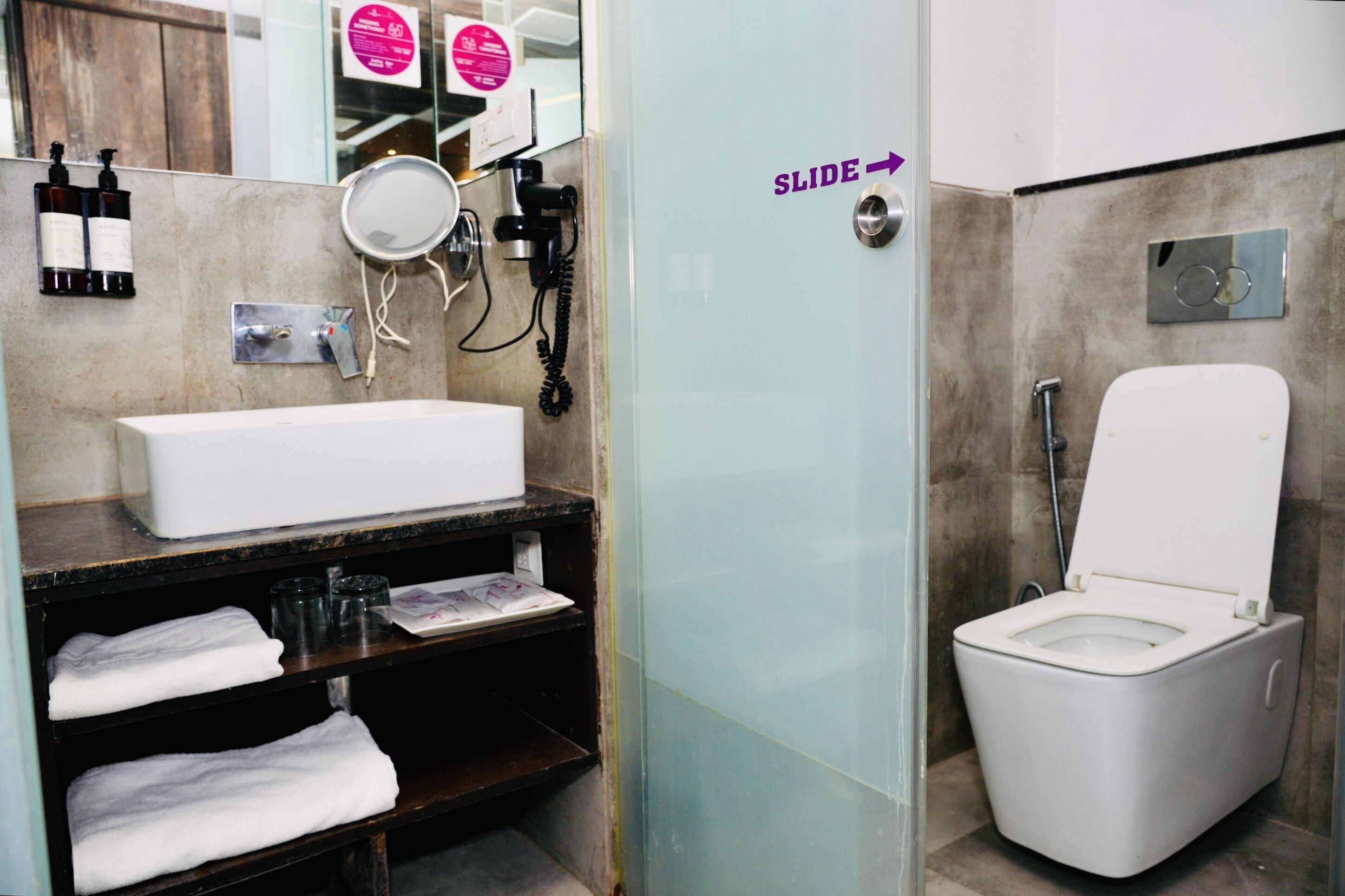 A bathroom with a white sink, mirror, and toilet. There is a sign on the wall that says "SLIDE" with an arrow pointing to the right.