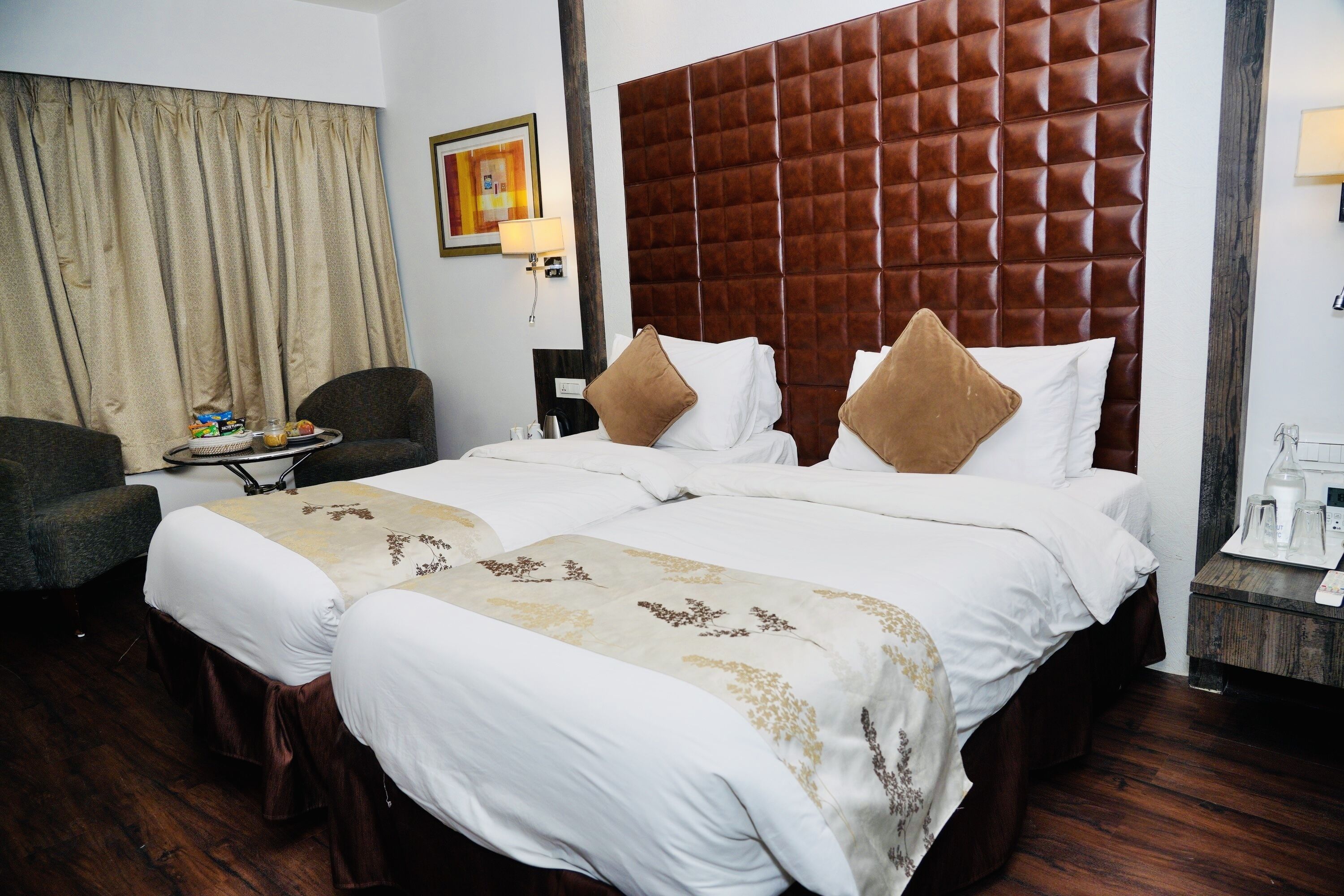 A hotel room with a large bed, two pillows, a bedside table, a chair, and a curtain.