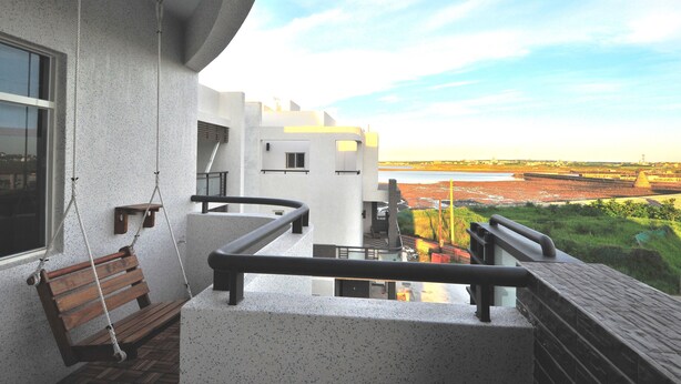 Un balcón con una hamaca de madera, vista a un río y un edificio moderno al fondo.