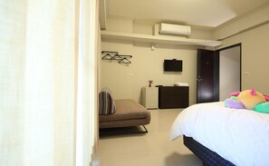 A hotel room with a bed, a small sofa, a desk with a chair, a TV, and an air conditioning unit. - A-Ba Homestay  (Hualien City)
