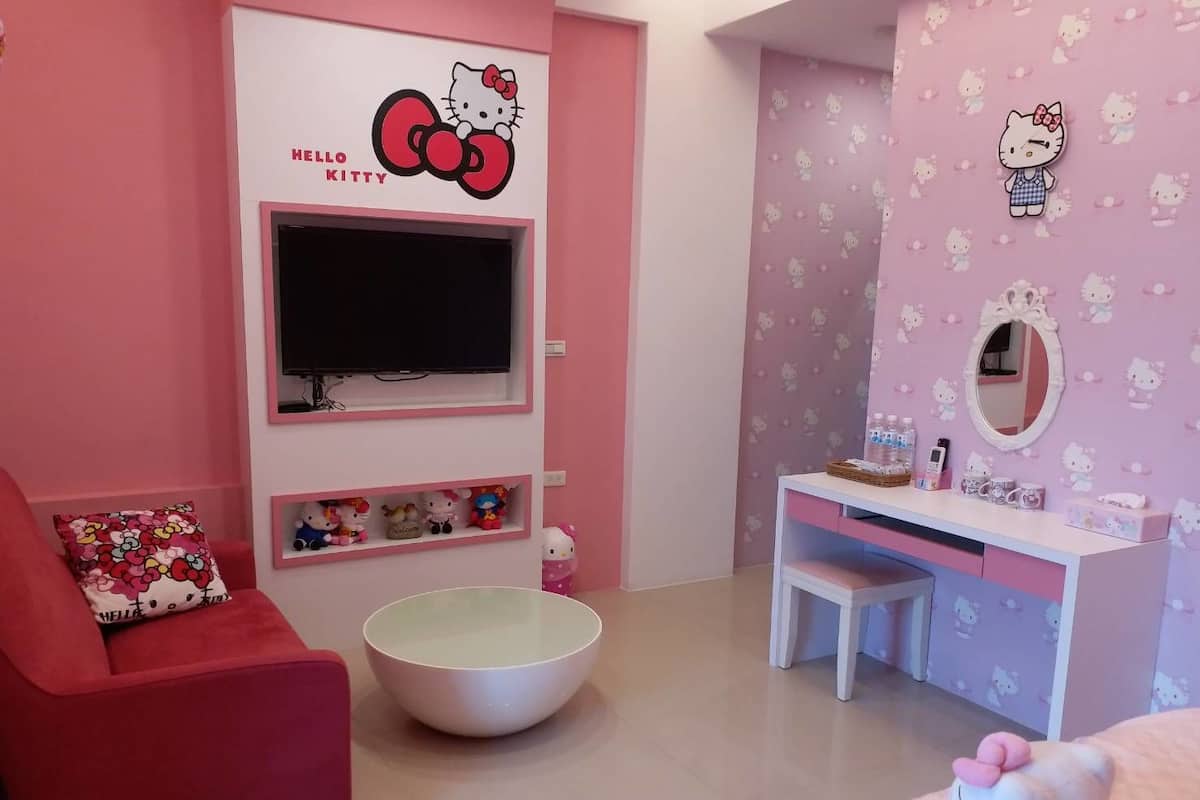 A pink-themed room with a red sofa, a white TV unit, a white desk, and a Hello Kitty-themed wall.