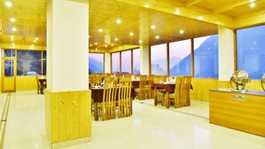 A restaurant with wooden interiors, large windows, and a mountain view. - Whistling Pines Resorts and Spa (Manali)