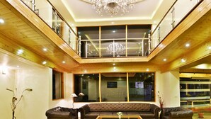 A spacious living area with a high ceiling, a chandelier, a large window, and a balcony. - Whistling Pines Resorts and Spa (Manali)