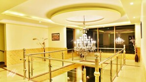 A spacious lobby with a glass railing, a grand chandelier, and a large window offering a view of the interior. - Whistling Pines Resorts and Spa (Manali)