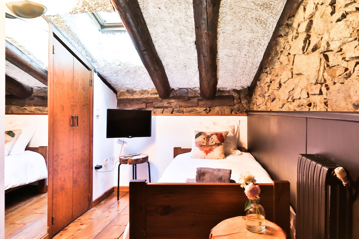 A bedroom with a wooden bed, a TV mounted on the wall, and a stone wall.