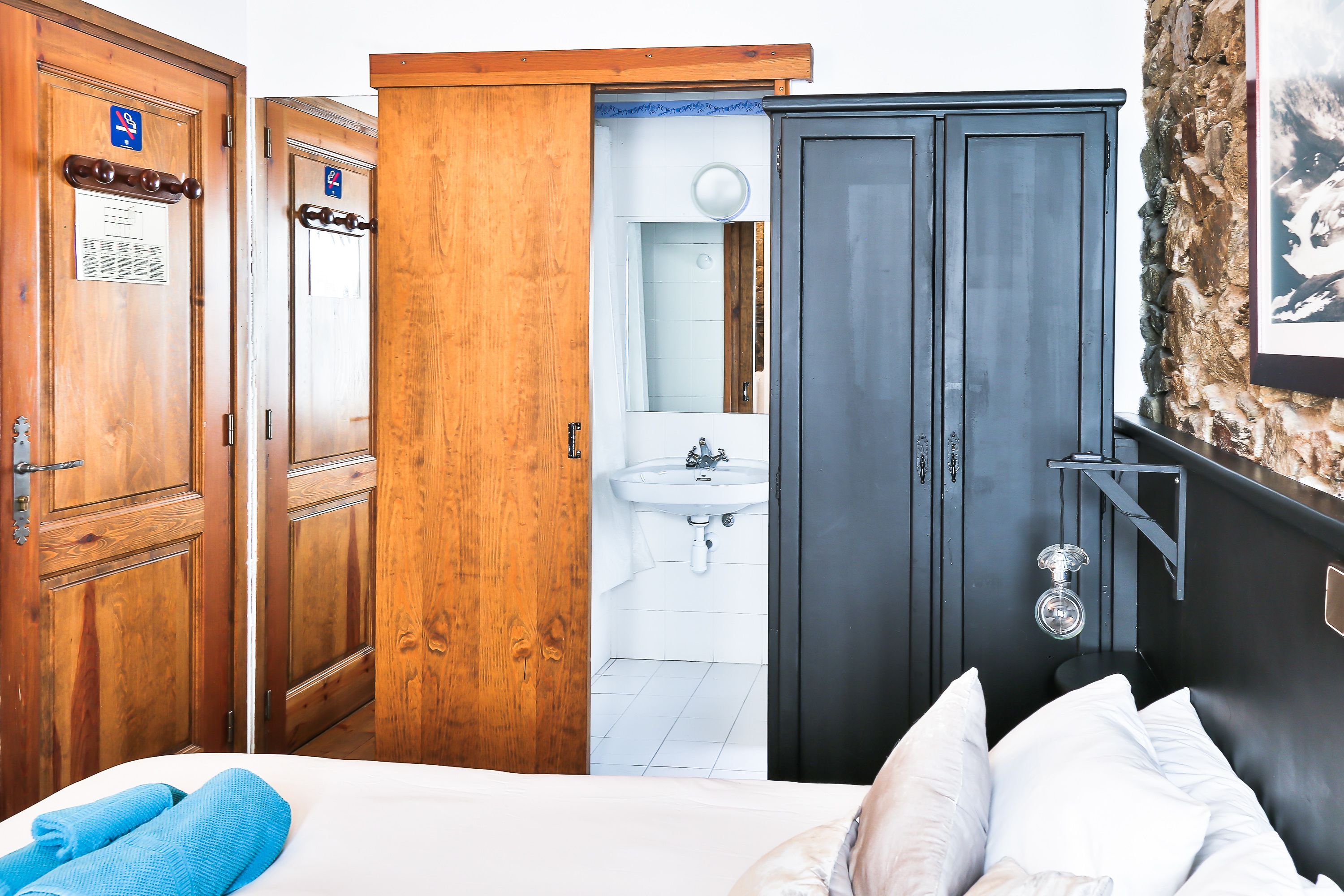 A hotel room with wooden doors, a white sink, and a bed with white and blue linens.