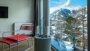 Une pièce avec une grande fenêtre, un fauteuil rouge, un radiateur blanc et une table en verre.
