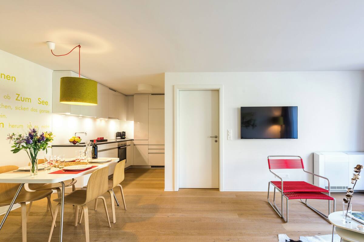 A modern kitchen with white cabinets, a dining area with a table set for two, and a red chair.