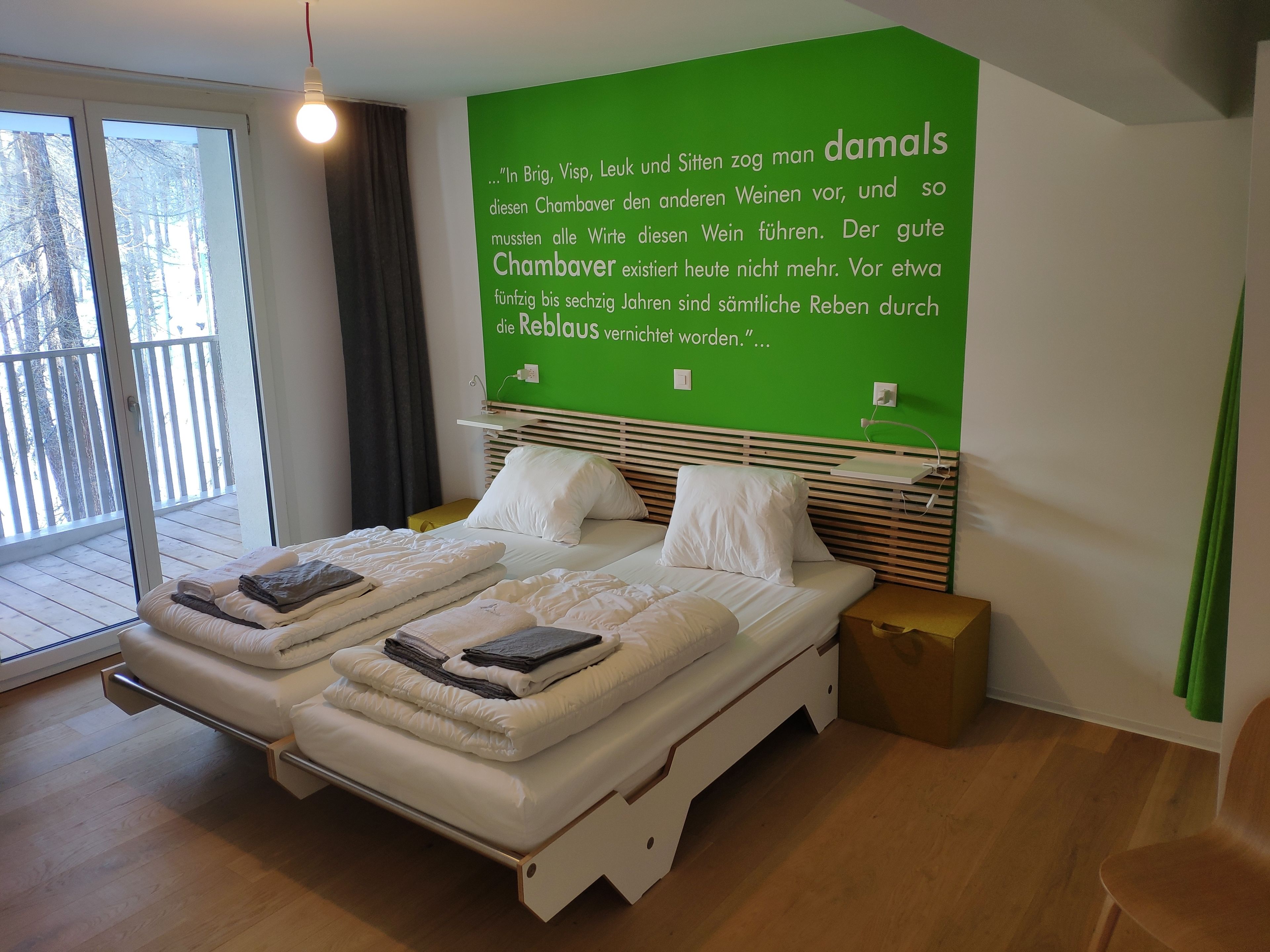 Une chambre moderne avec un mur vert, un lit avec une literie blanche et une vue sur un balcon.