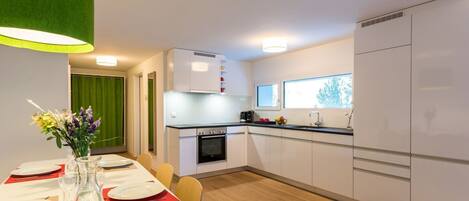 A modern kitchen with white cabinets, a built-in oven, and a refrigerator. There is a dining table set with plates and a vase of flowers.