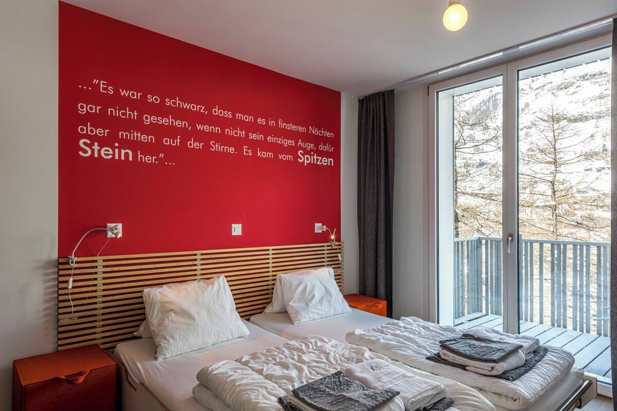 A hotel room with a large window, a red wall with text, and two beds with white bedding.