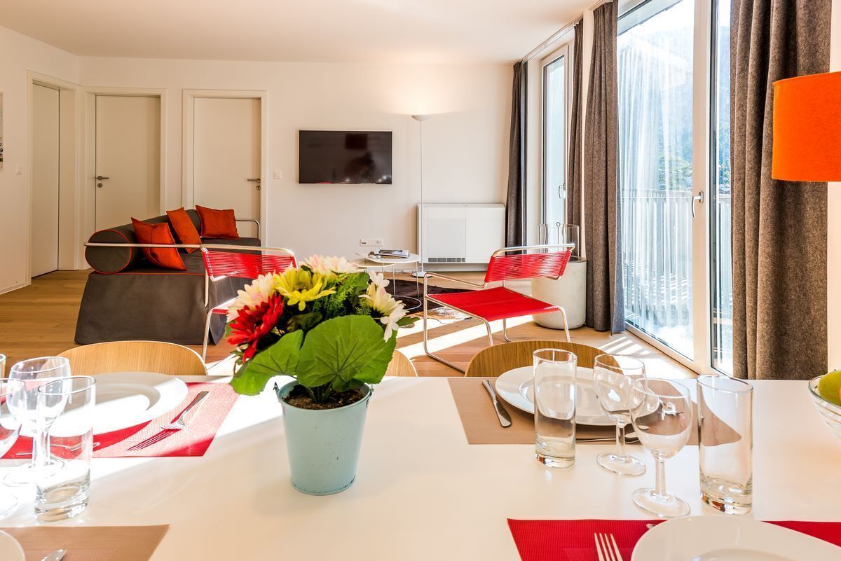 Een moderne woonkamer met een eethoek, grote ramen en een flatscreen televisie.