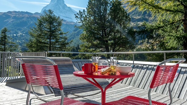 Une terrasse avec des chaises rouges et une table, d’où l’on a une vue sur une montagne.
