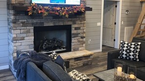 Una sala de estar con chimenea de piedra, un televisor de pantalla plana montado encima y un rincón de descanso acogedor con sofá y mesa de centro.