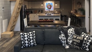 Un interior acogedor con un entrepiso con dormitorio, una zona de comedor y una sala de estar con sofá y cojines decorativos.