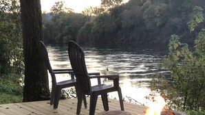Una terraza con dos sillas que da a un lago, una fogata y una parrilla.