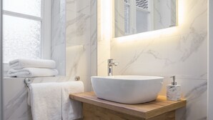 Ein Badezimmer mit einem weißen Marmorwaschbecken, einem Holzschrank darunter und einem Spiegel darüber.