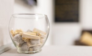 A clear glass bowl containing white stones and wooden sticks on a white surface.