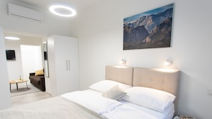 Ein modernes Schlafzimmer mit einem großen Bett, einem Wandbild von Bergen und einem kleinen Tisch mit einem Buch.