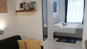 Ein modernes Hotelzimmer mit einer schwarzen Couch, einem runden Holztisch, einem Bett mit weißer Bettwäsche und einem großen Spiegel, der den Raum reflektiert.