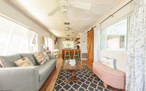 A cozy living room with a sofa, a pink ottoman, and a kitchen area with stools. - Super comfy cottage, close to the beach (Nokomis)