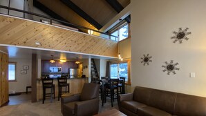 A spacious living area with a high ceiling, a kitchen in the background, and a staircase leading to an upper level.