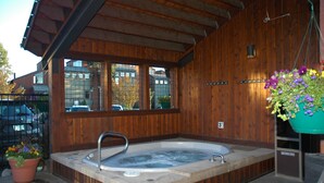 A wooden cabin with a hot tub, a window, and a potted plant.