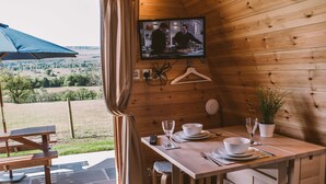 Een houten hut met een eethoek, een aan de muur bevestigde televisie en uitzicht op de omgeving.