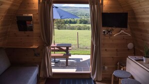 Een gezellig vakantiehuisje met houten inrichting, een bed, een bureau, een televisie en uitzicht op een groene omgeving door een groot raam.