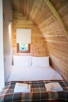 A cozy bedroom with a wooden sloped ceiling, a bed with white linens, and a plaid-patterned bedspread.