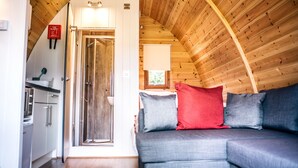 Een gezellig cabin interieur met houten plafond, een kitchenette, een douche en een grijze bank met rode en grijze kussens.